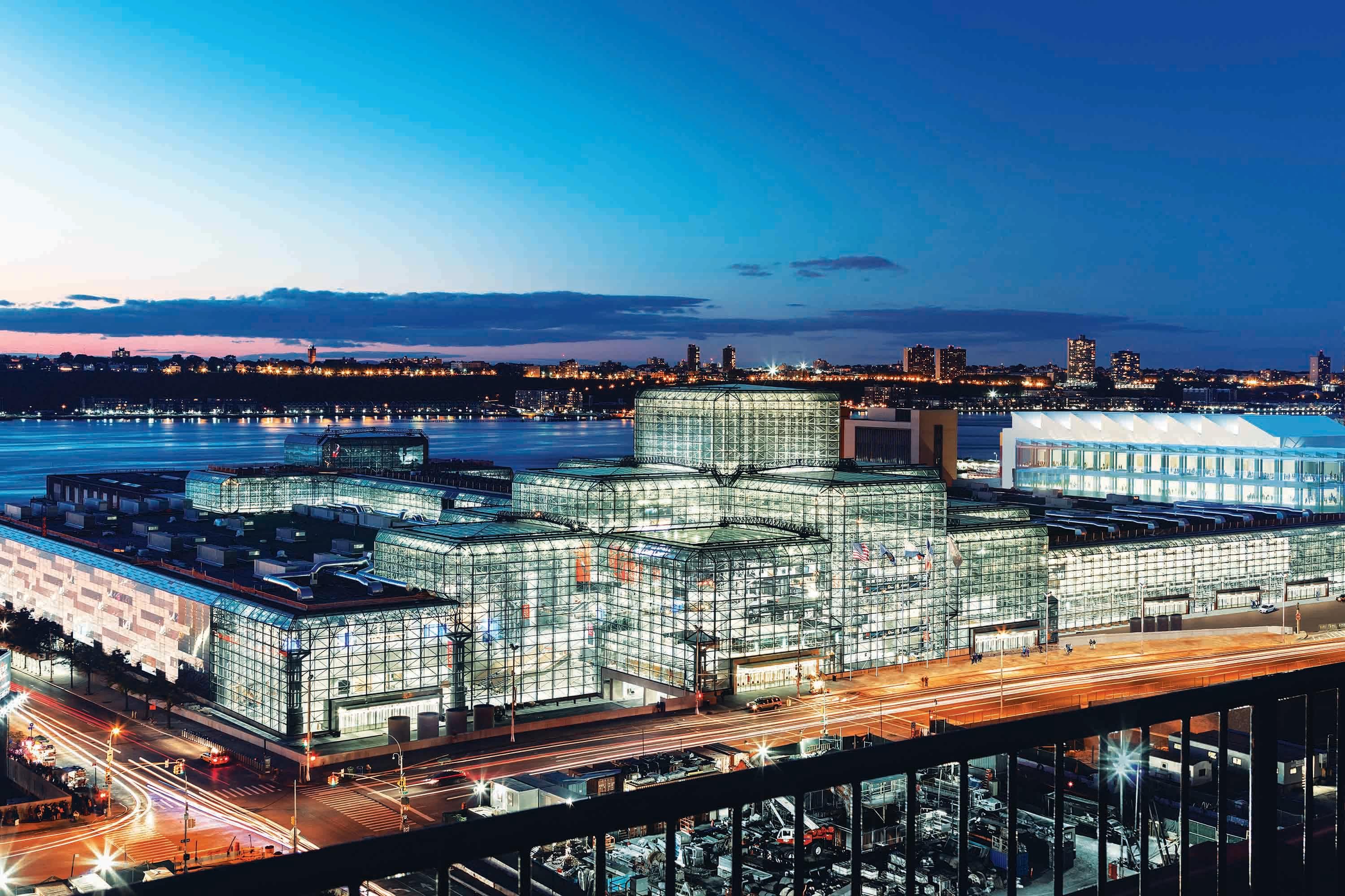 The illuminated glass facade of Javits Center beside the Hudson River at dusk